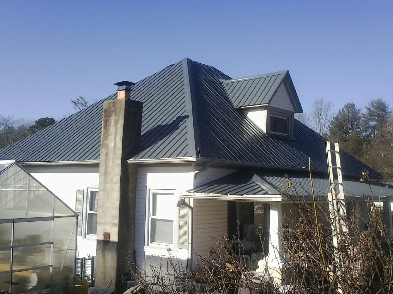 Dark blue standing seam metal roof on a white farmhouse with dormer — Slate & Tile Roof Repair by Roofing Brothers in Roaring Spring