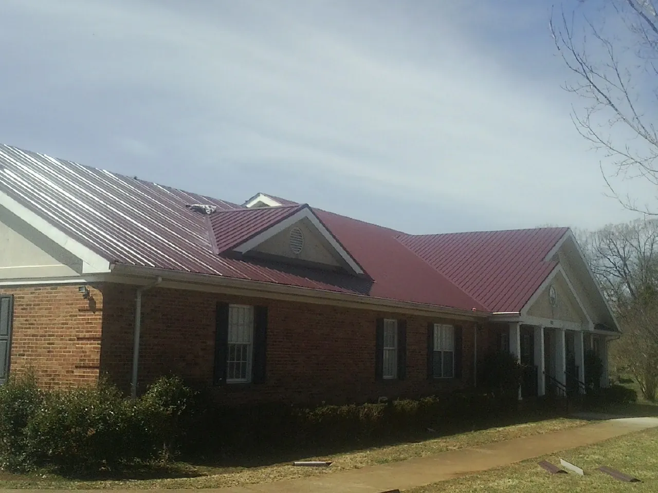 Red metal roof with gabled entries on a long brick building, from a Hail Damage Roof Repair job in Roaring Spring