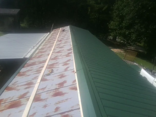 Old rusted panels beside newly installed green metal roofing — Wind Damage Roof Repair by Roofing Brothers in Roaring Spring