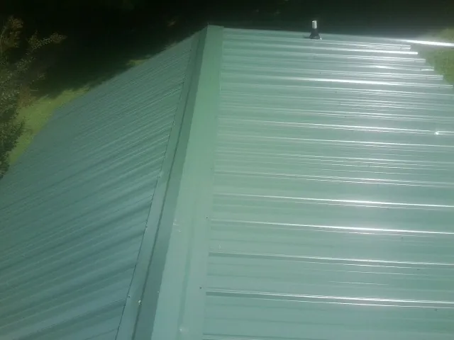 New green metal panels meeting at the ridge of a roof — Flat Roof Repair work by our crew in Roaring Spring