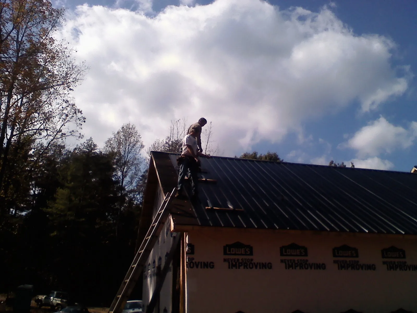 Roofer fastening dark metal panels high against a cloudy sky, from a Roof Inspection job in Roaring Spring