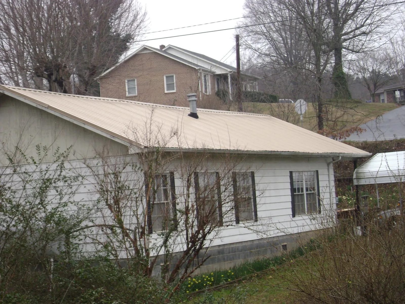 Tan metal roof on a white sided house set into a hillside — Commercial Roofing by Roofing Brothers in Roaring Spring